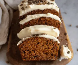 Delicious homemade pumpkin bread topped with creamy cream cheese frosting, garnished with fresh olives and thyme herbs