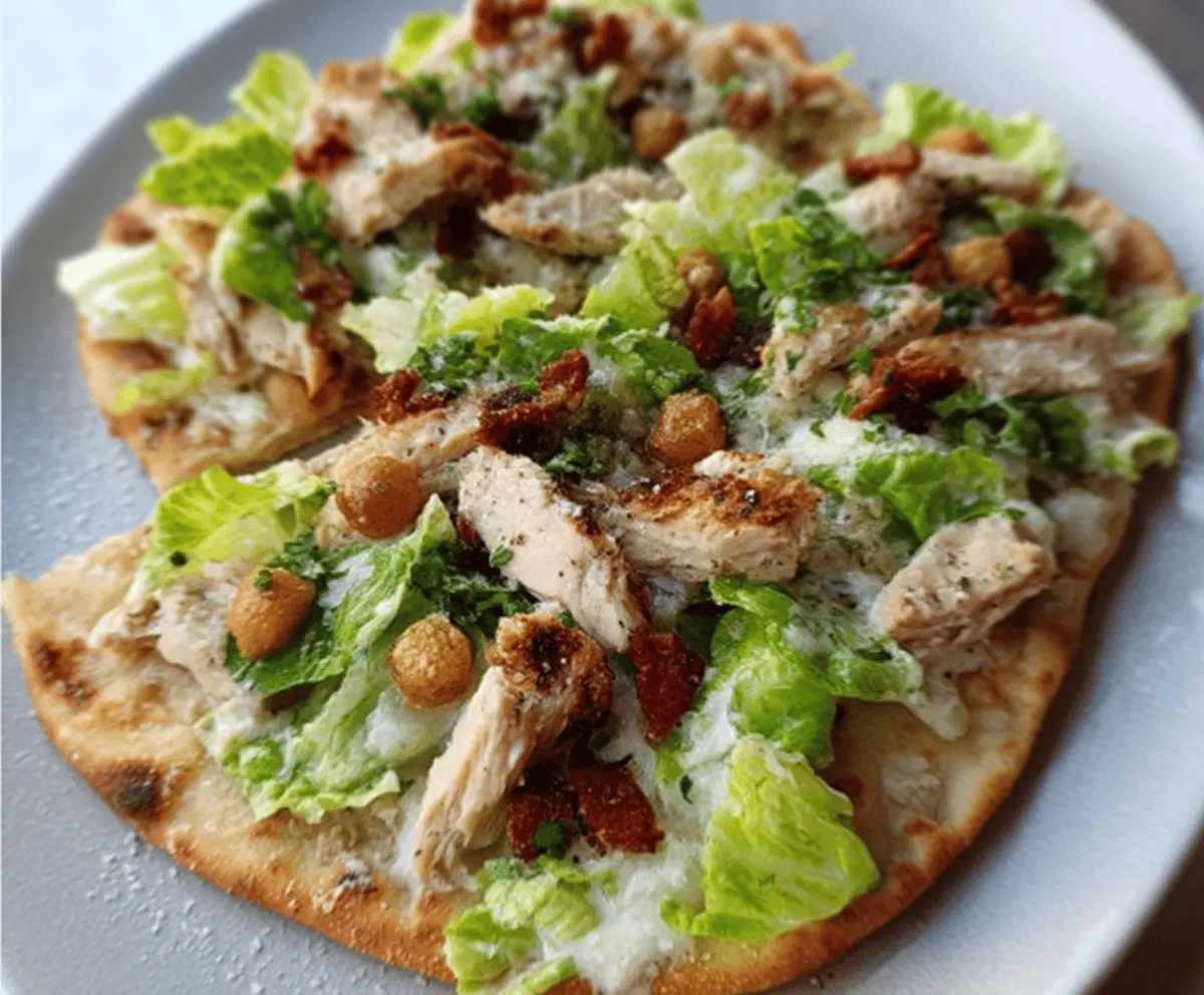 Close-up of delicious Chicken Caesar Flatbread with grilled chicken, fresh romaine lettuce, grated Parmesan cheese, and Caesar dressing on a crispy flatbread slice.
