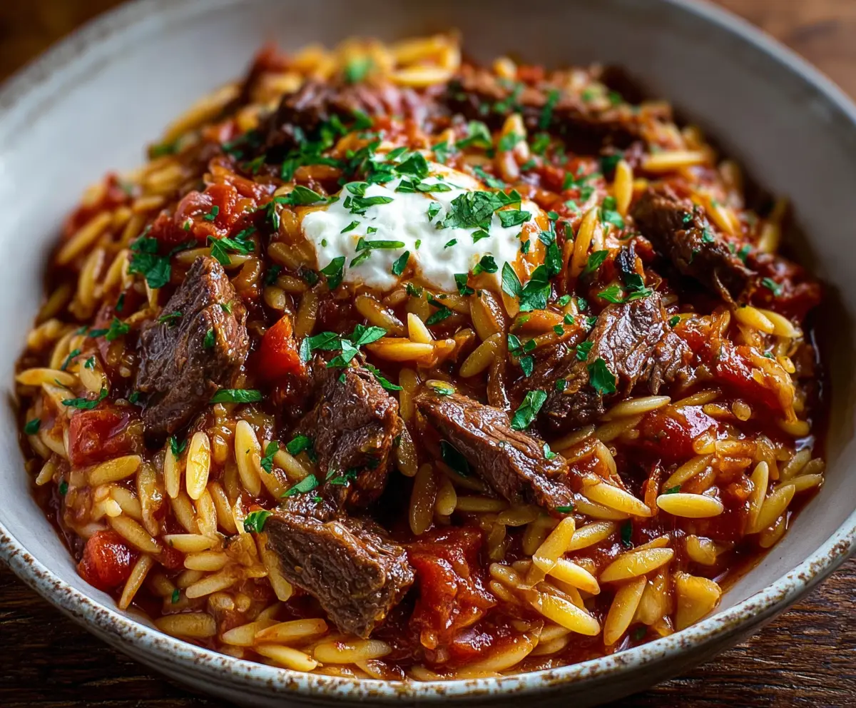 Delicious Beef Giouvetsi with Orzo in a rustic ceramic baking dish, garnished with fresh herbs.