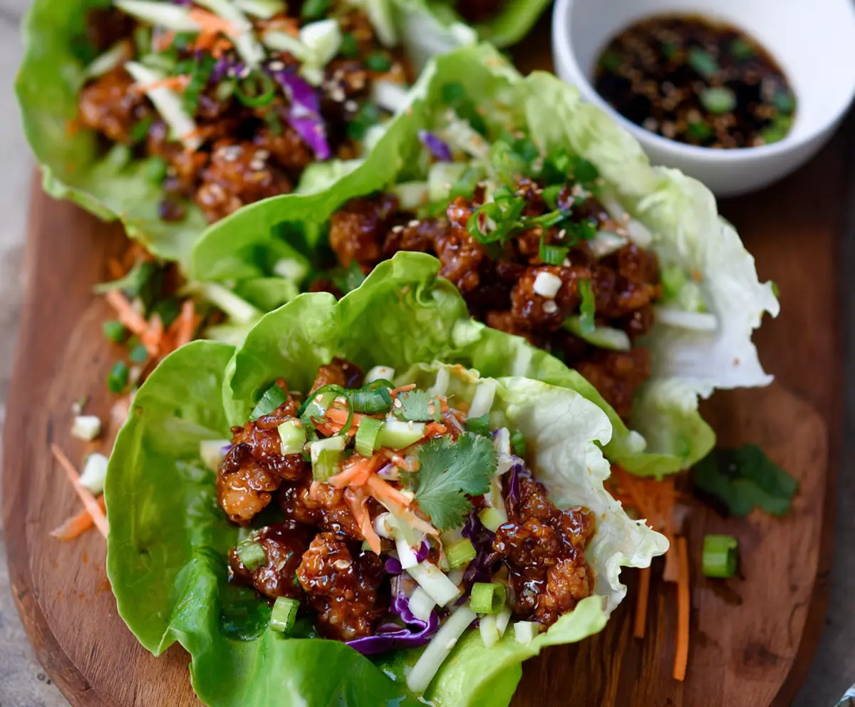 Hot Honey Chicken Lettuce Wraps garnished with fresh herbs on a white plate