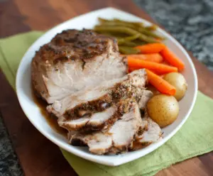 Juicy and tender pressure cooker pork roast garnished with herbs on a rustic plate.